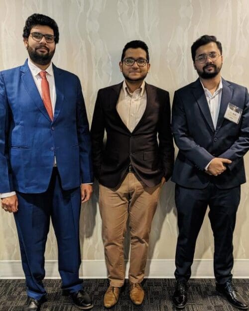 3 students in formal attire standing in a row against a patterned wall