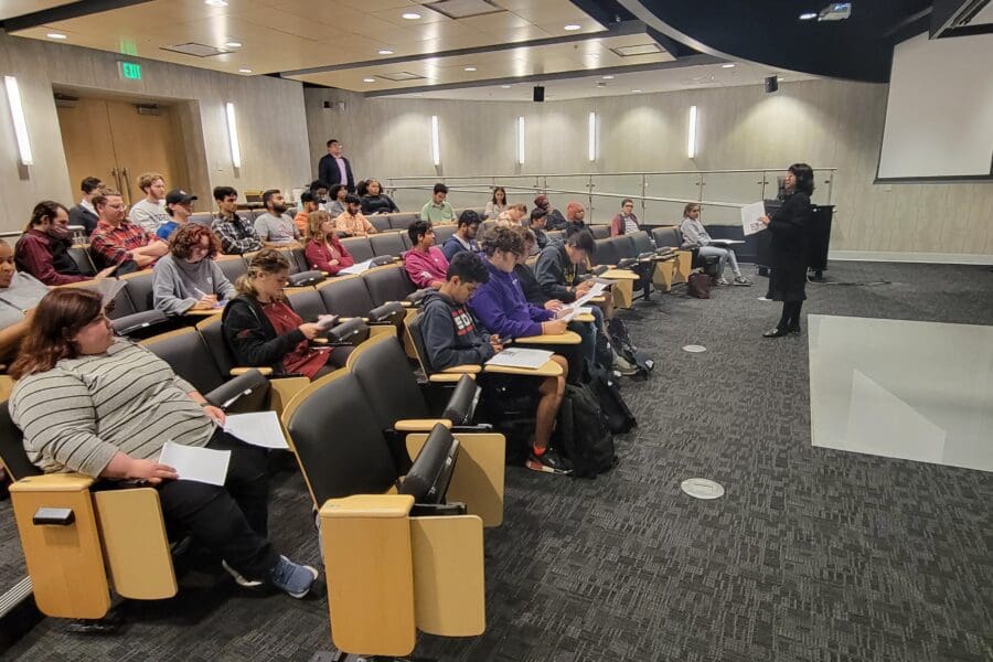 Woman standing in front of screen in auditorium with several people seated in rows of chairs