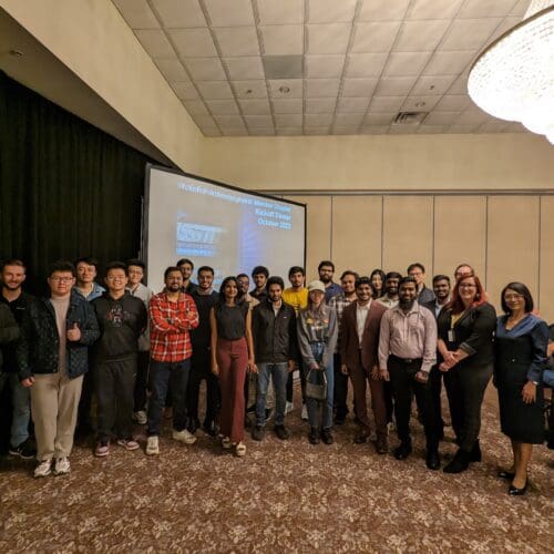 A large group of individuals in business professional attire stand together in front of a large screen.