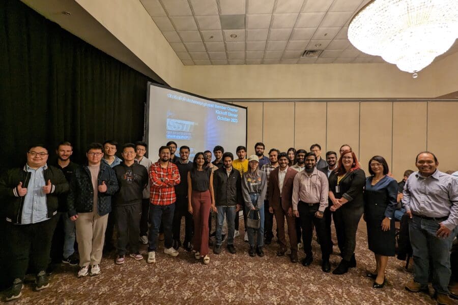 A large group of individuals in business professional attire stand together in front of a large screen.