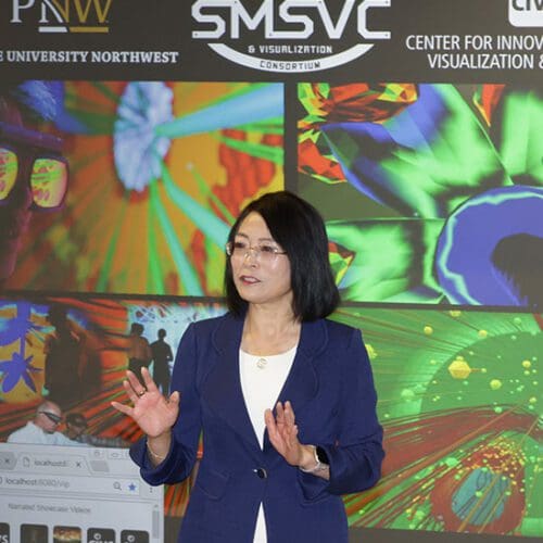 Chenn Zhou stands in front of a projection screen that shows images of blast furnace operations.