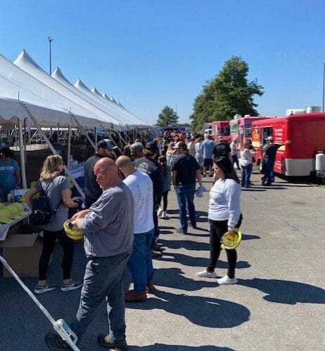 Several people attending an outdoor festival with a row of white tents and a row of red food trucks