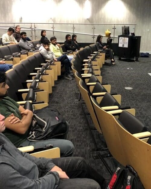 Woman standing in front of screen in auditorium with several people seated in rows of chairs