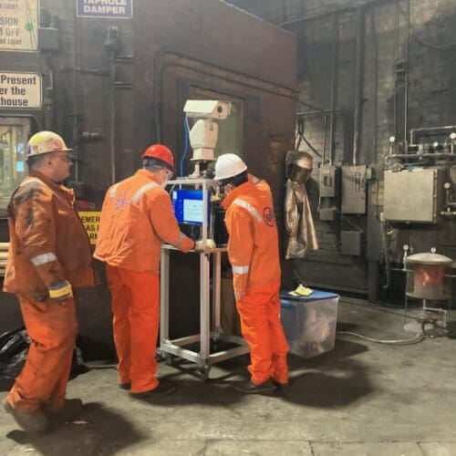 3 men in an industrial setting wearing bright orange uniform jumpsuits with USS on the back