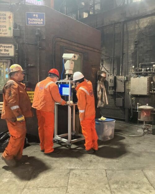 3 men in an industrial setting wearing bright orange uniform jumpsuits with USS on the back