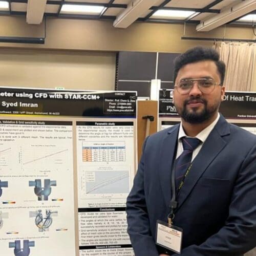 Young student in a navy suit standing in front of academic poster in presentation hall