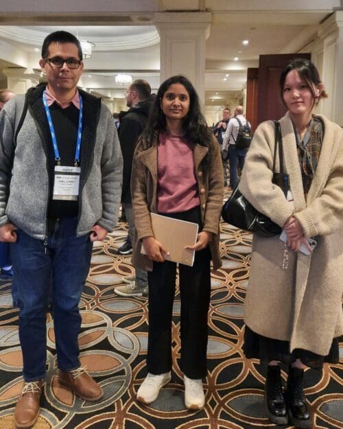 CIVS researchers Orlando Ugarte, Sathvika Kottapalli, and Shiyu Wang standing in a hallway of a convention center wearing special passes on lanyards