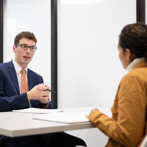 Two students in suits speak over a table.