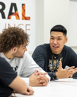 Three students sit at a table and talk to each other