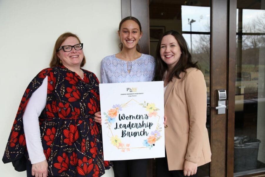 Three people with a Women's Leadership Brunch sign