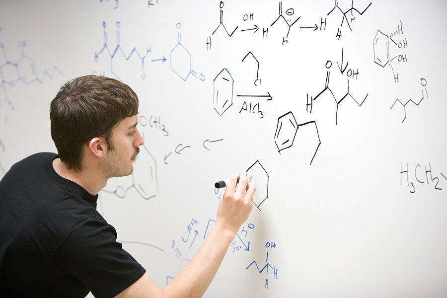 A student writes a chemistry equation on a white board.