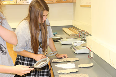 Two high school students analyze evidence with hand held magnifying glasses during a forensic science summer camp.
