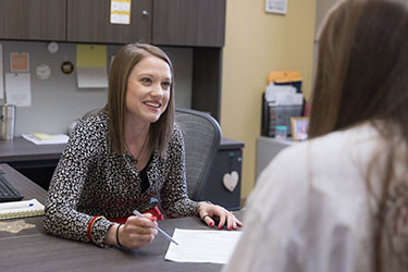 A student sits with Joelynn Stephen of the PNW Career Center. Joelynn is wearing an animal print blouse, pointing to a paper on her desk, and smiling at the student.