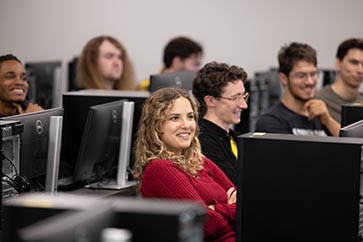 Classroom full of students on computers, while female in red shirt is smiling 363x242