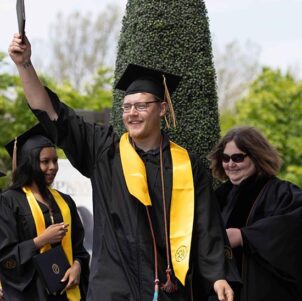 A student walks across the stage and holds up their diploma cover.