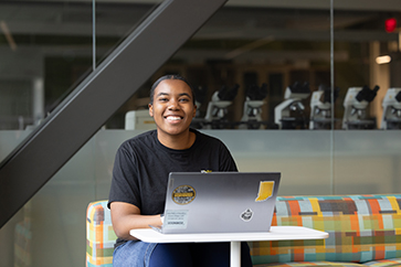 A student sits at a desk space with a laptop open in front of them.