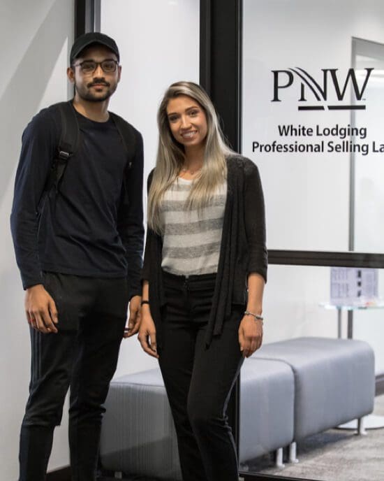 two standing students in front of PNW sign