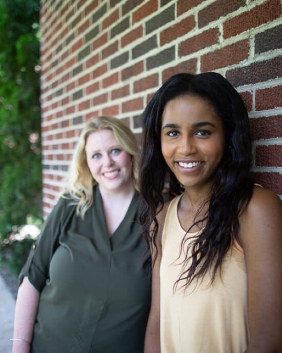two smiling students against brick wall