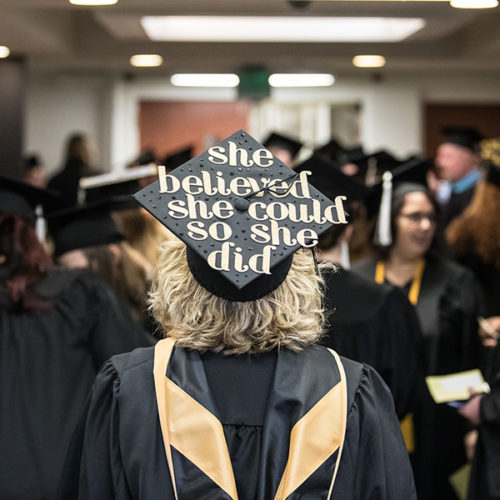 A PNW graduate in a crowd. Her cap reads "She believed she could so she did."