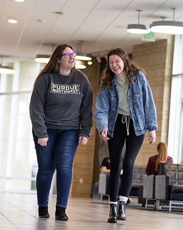 Two students walk down a hallway, both students are smiling and laughing