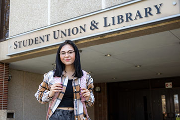 A Human Development and Family Studies major stands outside the Student Union and Library building