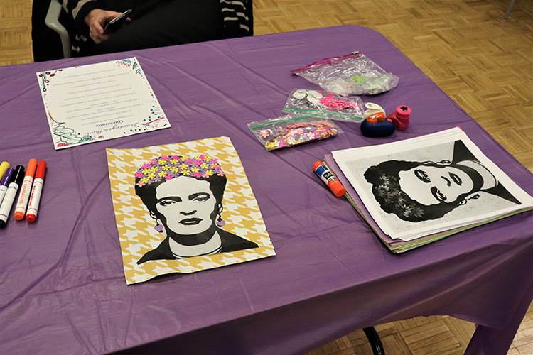 Printed drawings of Frida Kahlo sit on a table that is covered with a purple table cloth