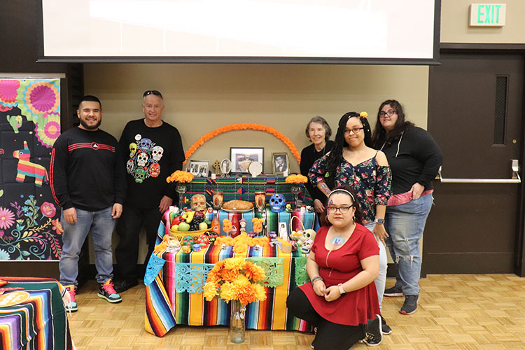 Six people pose around an ofrenda table set up for Day of the Dead