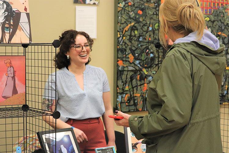 A student stands at a table and speaks to the person behind the table.