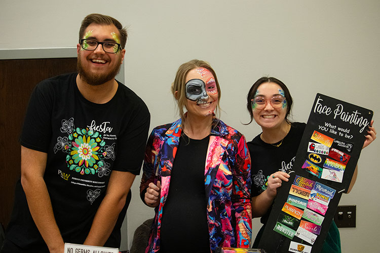 Two staff members and a face painting artist pose together. All three people have their faces painted.