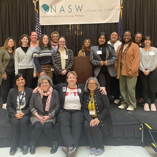 A group of students and faculty post on stage with members of the NASW leadership.