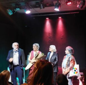 Jose Castro Urioste, Nora Ugartemendia, Maria Ines Martinez, and Graciela Balletti stand on stage in a spotlight.