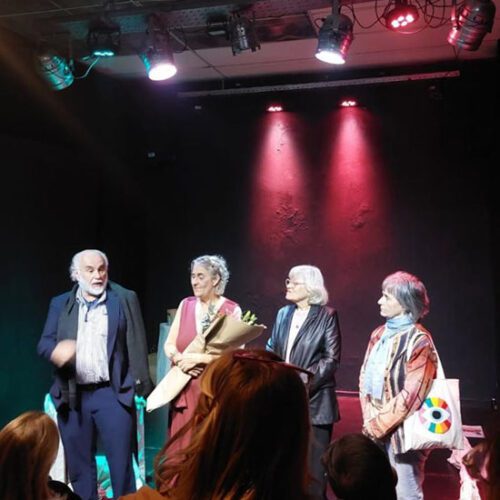 Jose Castro Urioste, Nora Ugartemendia, Maria Ines Martinez, and Graciela Balletti stand on stage in a spotlight.