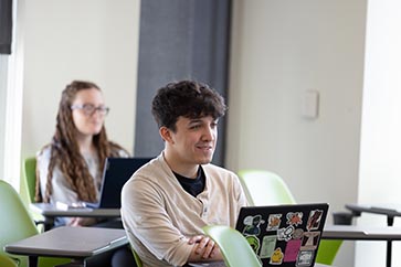 PNW student sitting at a desk with a laptop in front of him 363x242