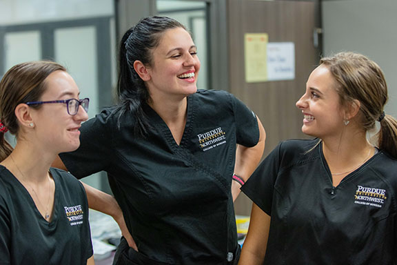 Three nursing students stand together, smiling, while wearing PNW scrubs