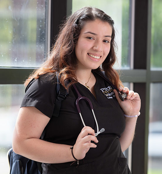 Student poses in scrubs with a stethoscope draped behind her neck