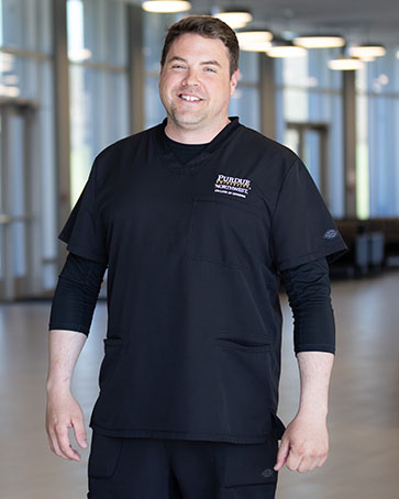Male student stands in a hallway, he is wearing black PNW College of Nursing scrubs