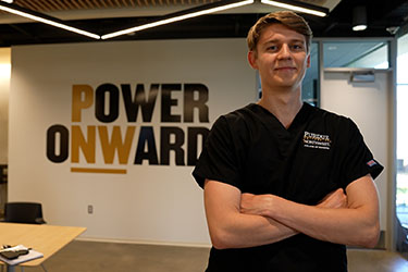A student in PNW scrubs stands with their arms crossed.