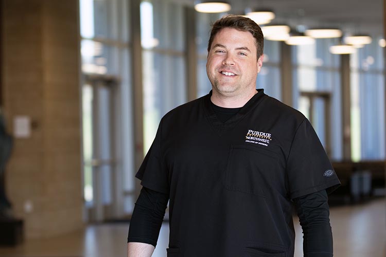 A PNW nursing student poses in branded scrubs