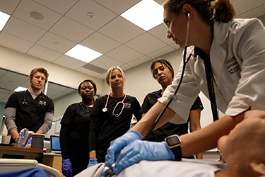 Four nursing students watching the professor teach with a mannequin