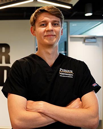 A student in PNW nursing gear stands with crossed arms in front of a Power Onward banner