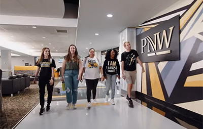 Purdue University Northwest Students Walk in Front of a PNW sign in Calumet Falls.