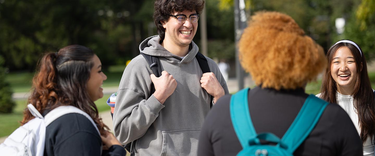 Four students talking with one another outside 1440x600