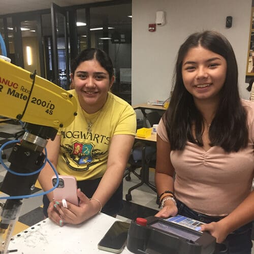 Two students smile next to a robot