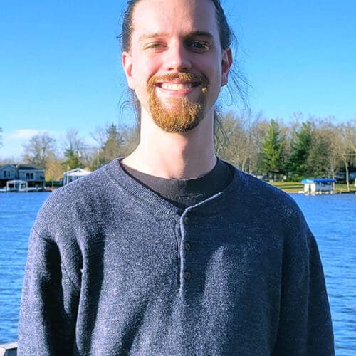 Fall 2022 PNW graduate Ryan Frederick stands in front of a lake.