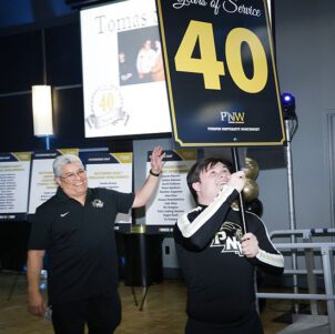 A PNW cheerleader walks in with a "40" sign to honor 40 years of service for lead service maintenance worker Tommy Sanchez at PNW Founders Day 2024.