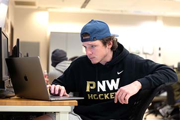 A student in a PNW sweatshirt works on a laptop computer.