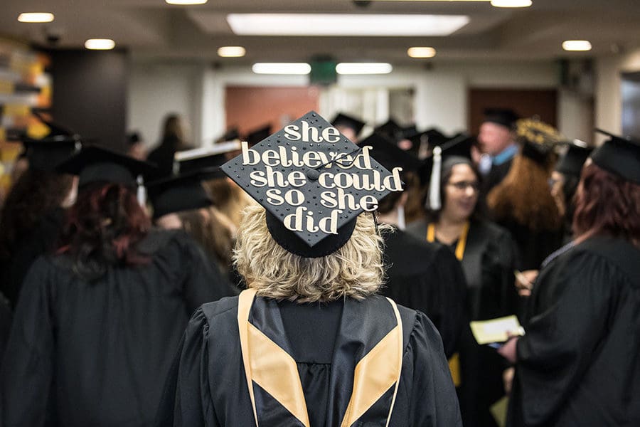 A PNW graduate in a crowd. Her cap reads "She believed she could so she did."