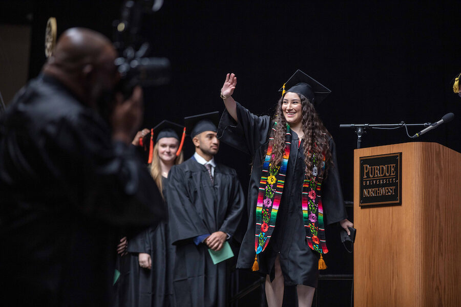 A graduate waves as she crosses the stage.