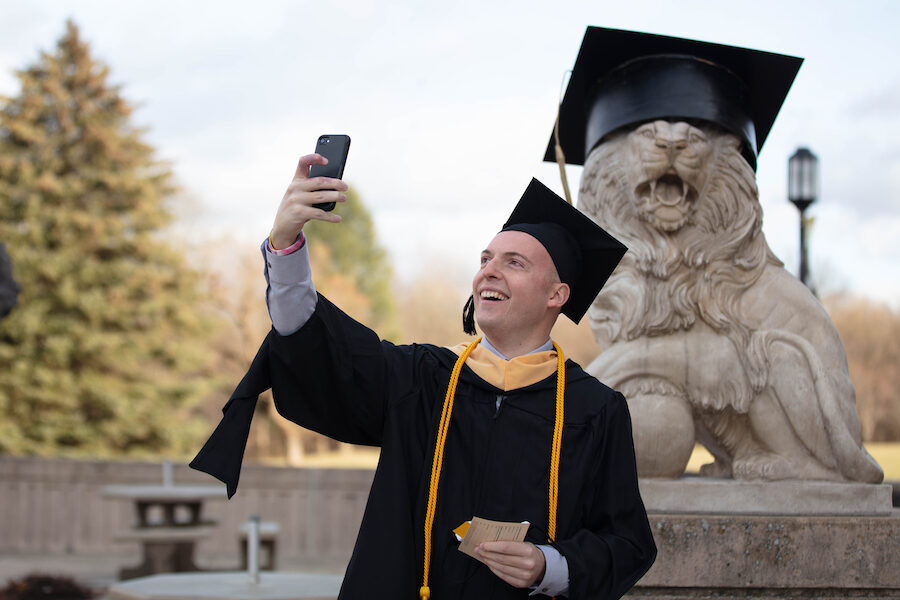 A grad takes a pic with the lion statue.