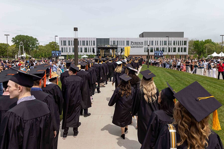 PNW graduates in regalia walk to the Nils K. Nelson Bioscience Innovation Building.